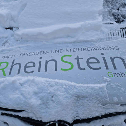 Das Firmenfahrzeug der RheinStein GmbH, das im Schnee steht, mit einer Folierung, die das Logo und den Schriftzug ‚Dach-, Fassaden- und Steinreinigung‘ zeigt